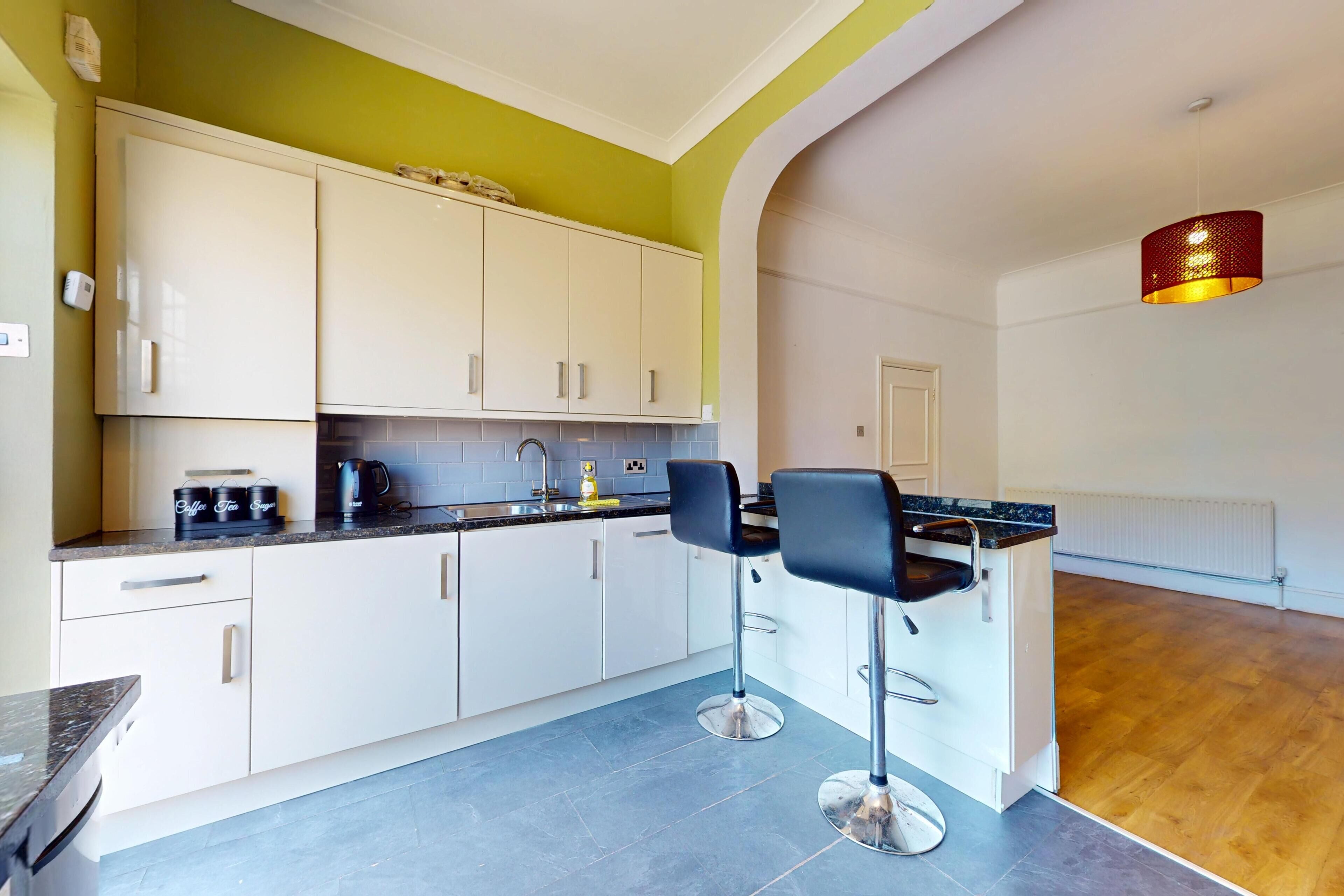 A modern kitchen with white cabinets, a black countertop, and two bar stools.
