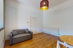 A room with a grey sofa, a wooden dining table, a white door, and a red and gold pendant light. - Amazing 2BR Flat with Garden-Easy Access to Camden (London)