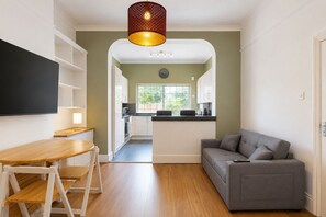 A modern living room with a grey sofa, wooden dining table, and a kitchen in the background. - Amazing 2BR Flat with Garden-Easy Access to Camden (London)