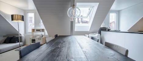 A modern loft apartment with a large dining table, a sofa, a lamp, and a kitchen area.