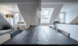 Eine moderne Loftwohnung mit großem Esstisch, einer Couch, einer Lampe und einer Küchenzeile.