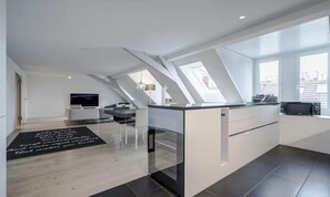 Eine moderne Küche mit einer großen Kochinsel, einem Essbereich mit einer Couch und einem Fernseher im Hintergrund.