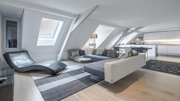 Eine moderne Loftwohnung mit hohen Decken, Dachfenstern, einer Couch, einer Liege und einer Küchenzeile.