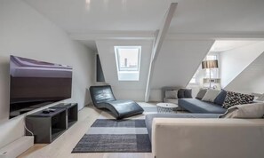 En moderne stue i loftstil med et fjernsyn, en lænestol, en sofa og et lille rundt bord.