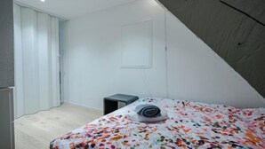 Ein Schlafzimmer mit einem Bett, einem kleinen Nachttisch, einem Heizkörper und einer weißen Tür.