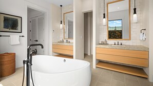 Un bagno moderno con una vasca freestanding, due lavabi con specchi e un'ampia finestra.