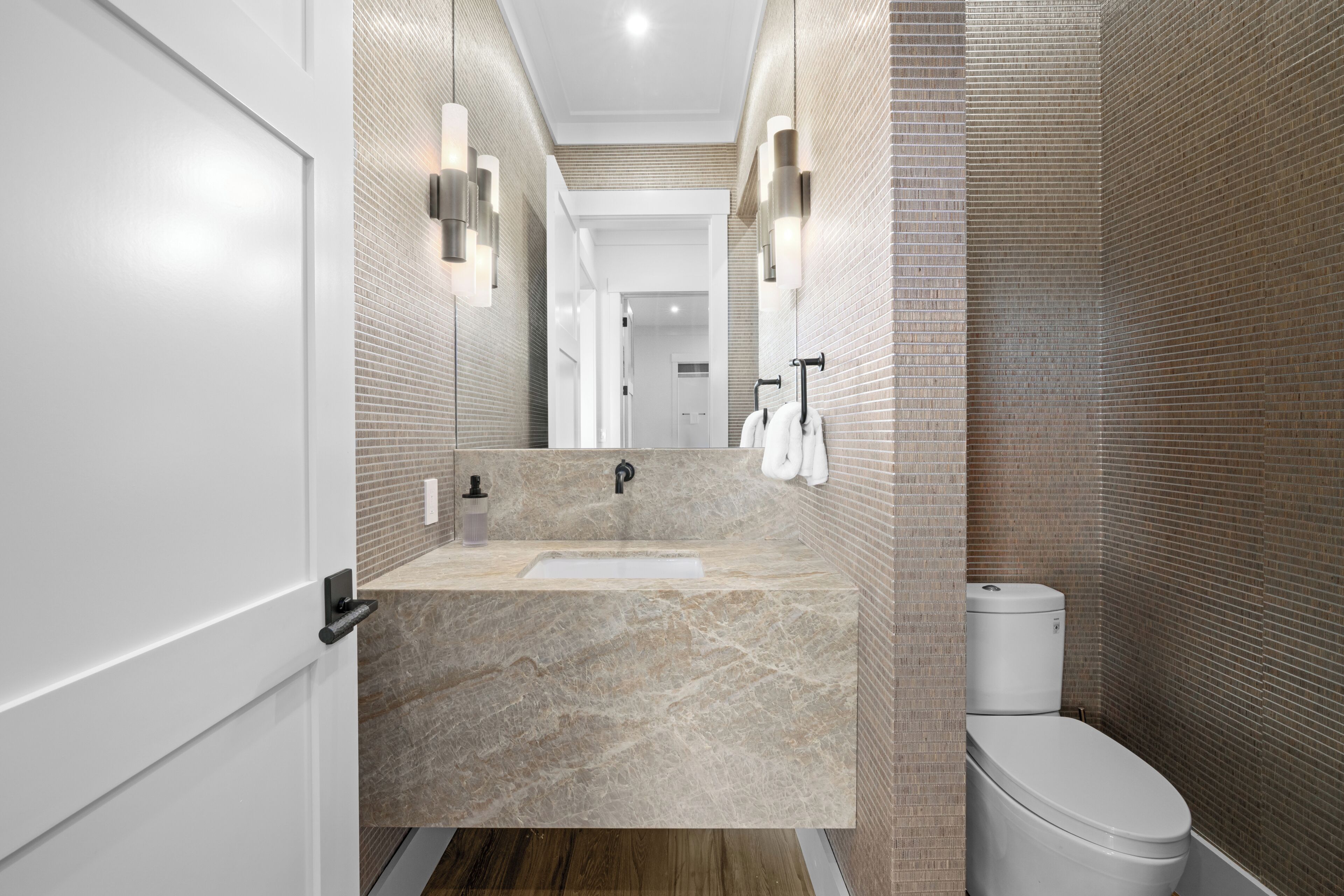A modern bathroom with a marble sink, a toilet, and a mirror with wall-mounted lights.
