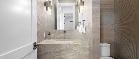 A modern bathroom with a marble sink, a toilet, and a mirror with wall-mounted lights.