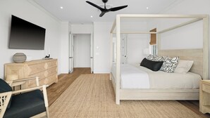 Una camera da letto moderna con un letto a baldacchino, una TV a schermo piatto, un comò in legno e una ventola a soffitto.