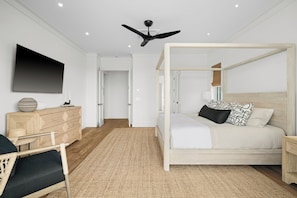 A modern bedroom with a four-poster bed, a flat-screen TV, a wooden dresser, and a ceiling fan. - Makani Kai by Gather: Brand-New Luxury Home w/ Private Pool & Spa, AC, Chef’ (Koloa)