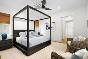 A four-poster canopy bed with a dark frame, a ceiling fan, and a framed landscape painting on the wall. - Makani Kai by Gather: Brand-New Luxury Home w/ Private Pool & Spa, AC, Chef’ (Koloa)