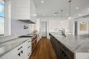 A modern kitchen with white cabinetry, a central island, and pendant lighting. - Makani Kai by Gather: Brand-New Luxury Home w/ Private Pool & Spa, AC, Chef’ (Koloa)