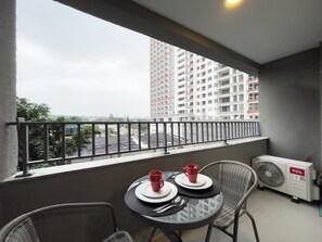 A balcony with a table set for two, a fan, and a view of a high-rise building. - Today Butantã  (São Paulo)