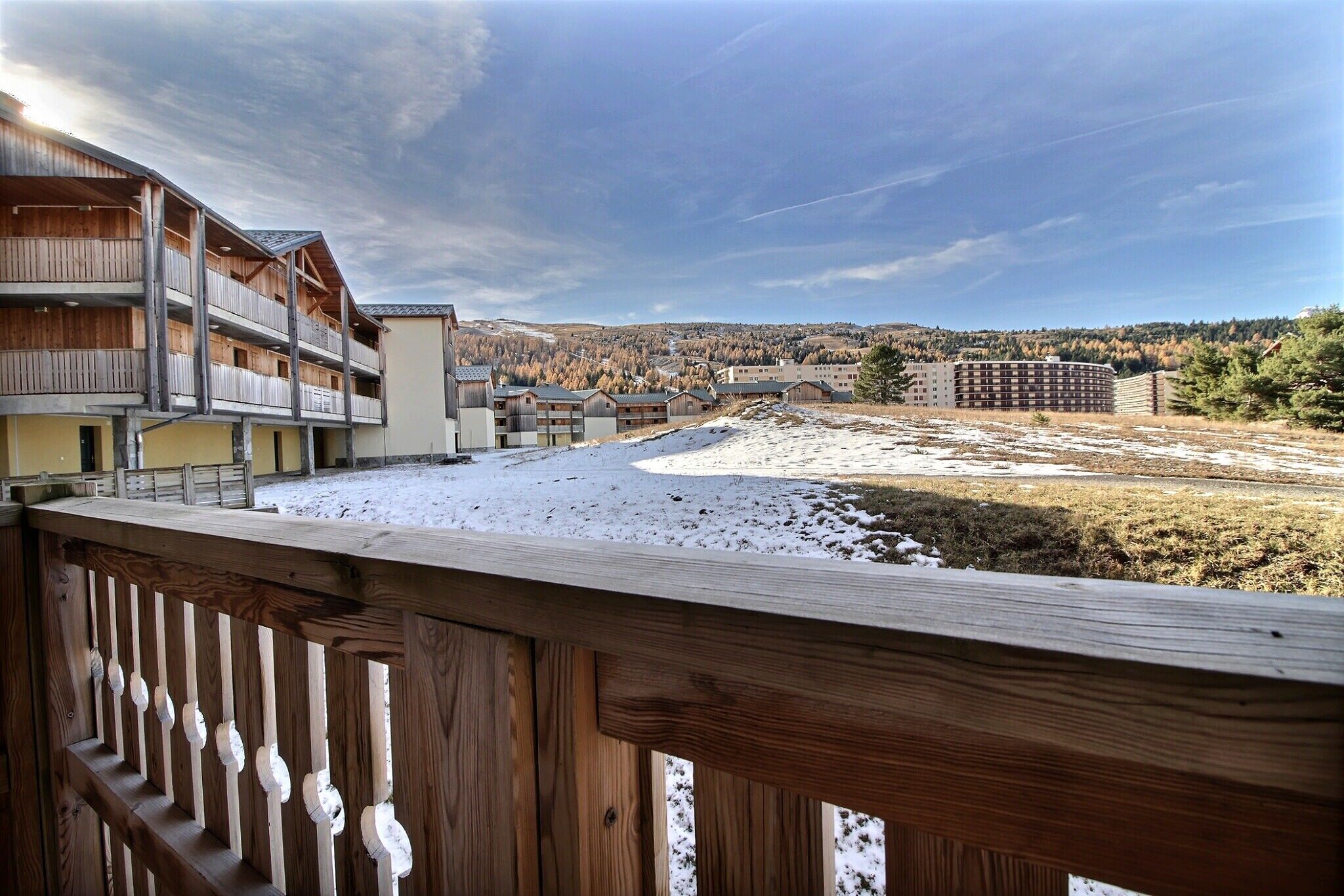 Un balcon en bois offrant une vue sur un paysage enneigé et sur des bâtiments situés au loin.