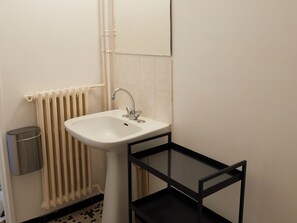 Ein Badezimmer mit einem weißen Waschbecken, einer schwarzen Metallablage und einer Heizung.