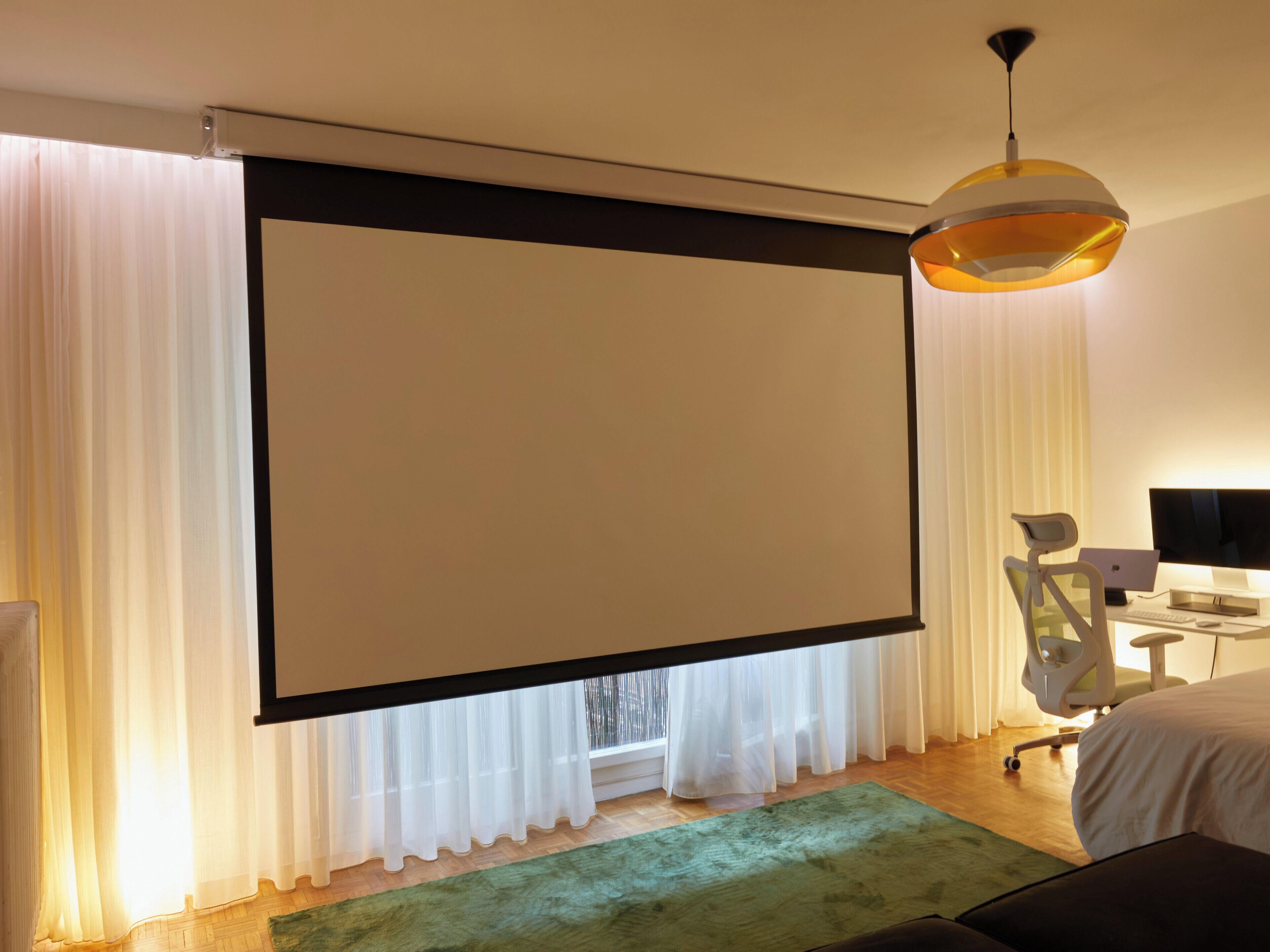 Une chambre avec un grand lit, un bureau avec un ordinateur, une chaise et un écran de projection.