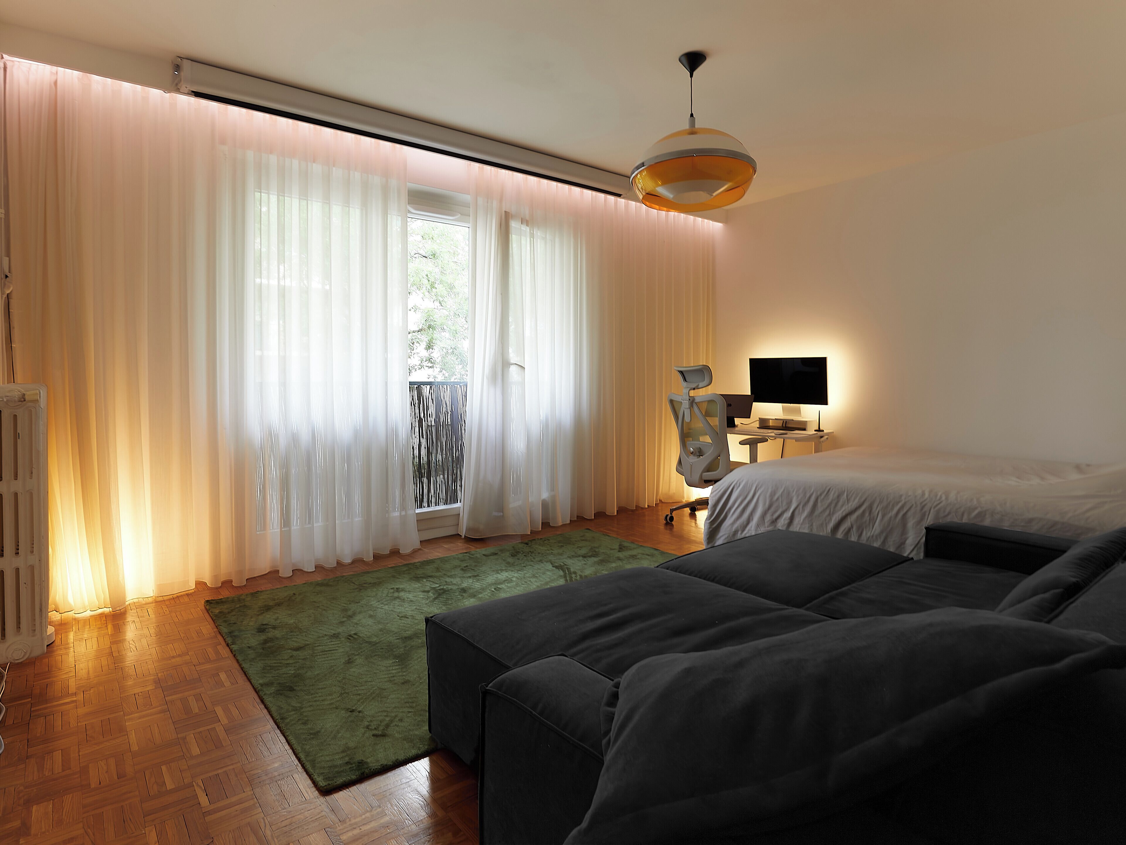 Ein modernes Schlafzimmer mit einem Bett, einem Schreibtisch mit Computer und einem grünen Teppich.