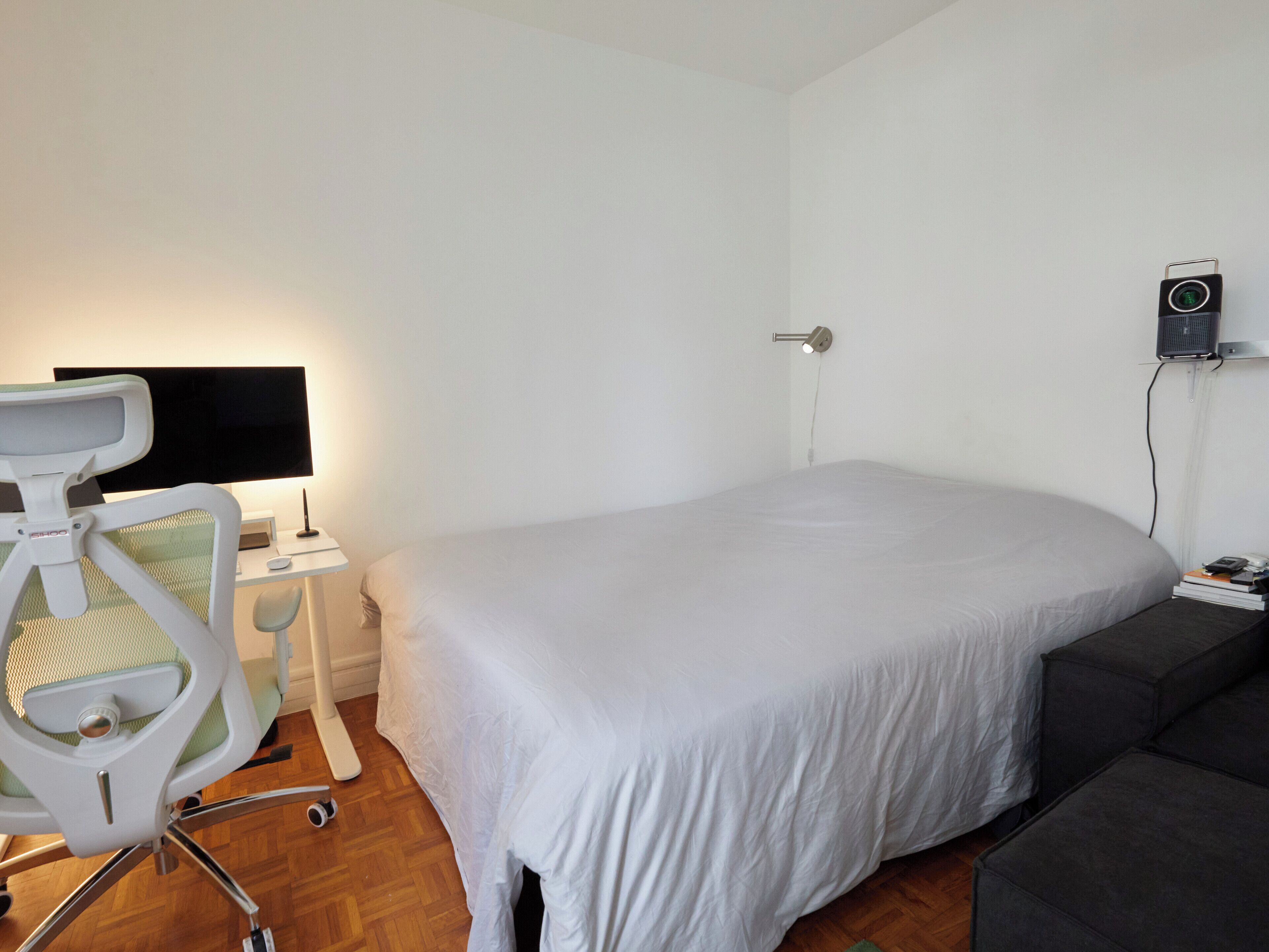 A bedroom with a bed, a desk with a chair, a flat-screen TV, and a wall-mounted speaker.