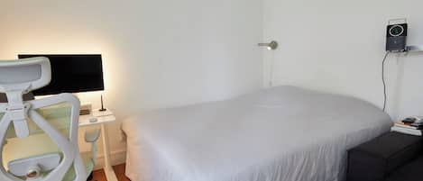 Un dormitorio con cama, un escritorio con silla, un televisor de pantalla plana y un altavoz instalado en la pared.