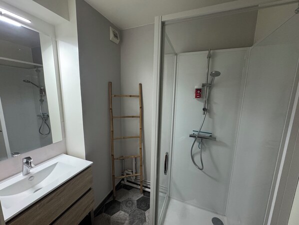 Baño con lavamanos blanco, espejo, ducha e una escalera de madera.