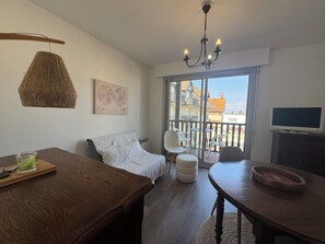 Ein Zimmer mit einem Bett, einem Holztisch, einem Esstisch, einer Chandelüster und Blick durch eine Glastür.