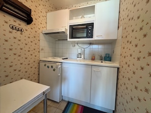 Eine kleine Küche mit Mikrowelle, Kaffeemaschine und Kühlschrank.