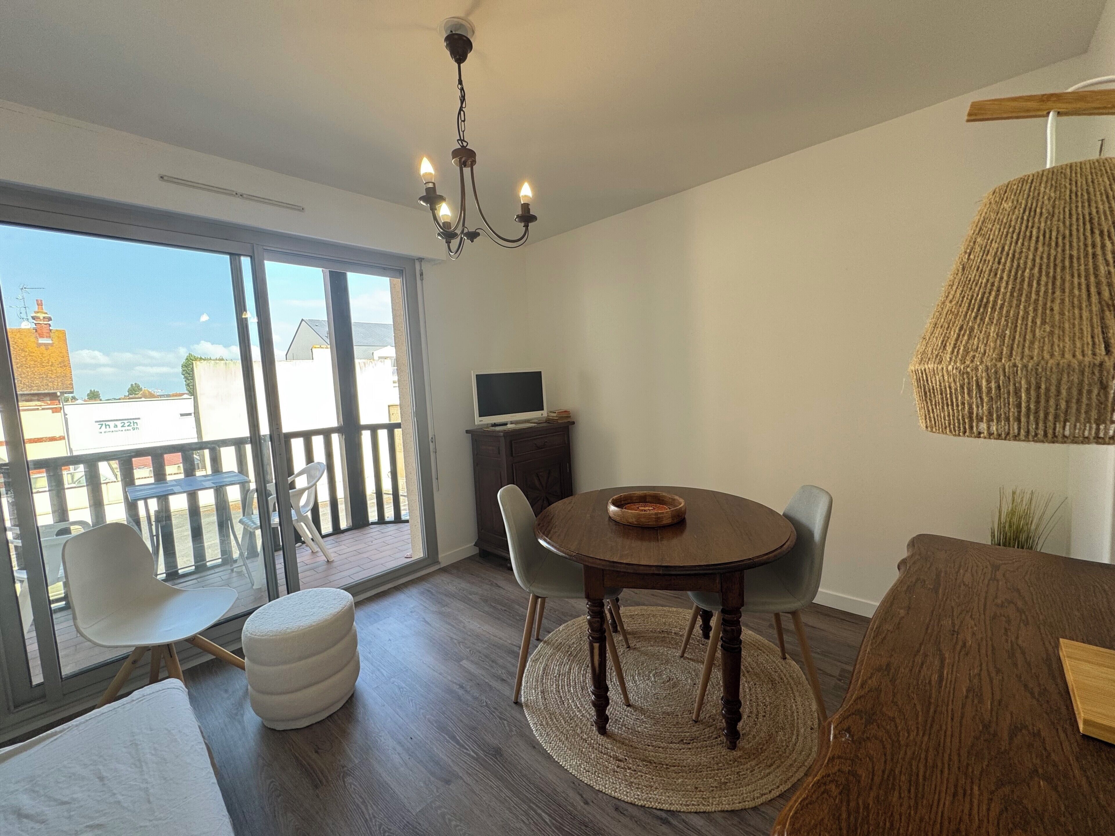 Ein modernes Wohnzimmer mit großem Fenster, einem runden Holzesstisch und einer Chandelier.