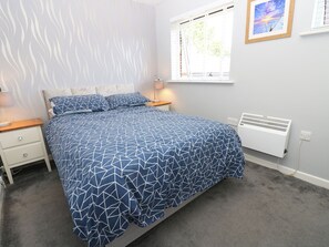 A bedroom with a bed, bedside tables, a window, a radiator, and a wall with a painting. - 73 Pennywell Gardens (New Milton)