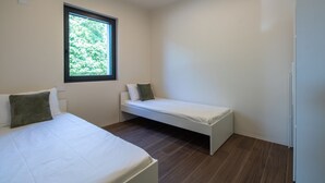 Un dormitorio con dos camas, una ventana y una pared blanca.