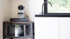 Una cocina compacta con microondas, cafetera y hervidor en un estante, con un ventanal sobre el fregadero.