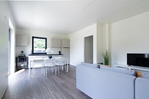 A modern living room with a grey sofa, a flat-screen TV, and a dining area with white chairs and a table. - A bright and welcoming 50-square-meter apartment, perfect for six people, located on the ground floor of a newly built building.The property is situated in an extremely quiet area and enjoys a strategic location, allowing you to easily visit Valeggio sul (Venturelli-Fenili)