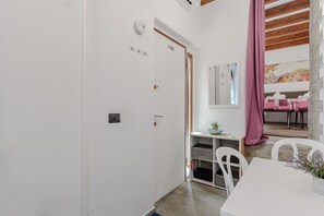 Una habitación con una puerta blanca, un escritorio pequeño con un espejo, una cortina rosa y una mesa con sillas.