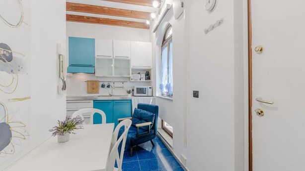 A compact kitchen with white cabinets, a blue chair, and a dining table. - A cozy 48 sqm apartment, ideal for up to 3 people, located on the ground floor of a building (accessible via one step).The property enjoys a strategic location, just 700 meters from Porta Nuova station and only 500 meters from the Marconi metro stop.It (Turin)