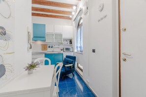Une cuisine de taille réduite avec des meubles blancs, une chaise bleue et une table à manger.