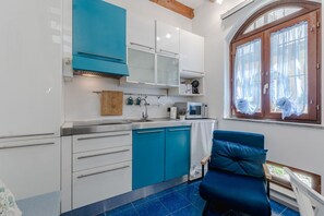 Una cocina compacta con armarios blancos y verde azulado, un microondas y una ventana con cortinas.