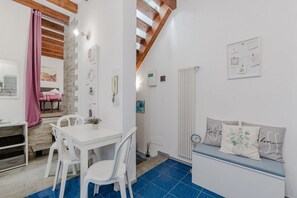 A room with a white table and chairs, a bench with cushions, a radiator, and a wooden ceiling beam. - A cozy 48 sqm apartment, ideal for up to 3 people, located on the ground floor of a building (accessible via one step).The property enjoys a strategic location, just 700 meters from Porta Nuova station and only 500 meters from the Marconi metro stop.It (Turin)