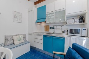 Cocina compacta con lavamanos, estufa y microondas. Hay una zona de estar con un banco y cojines.
