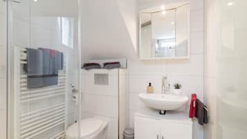 A modern bathroom with a glass shower enclosure, a white toilet, a vanity with a sink, and a mirror above the mirror.