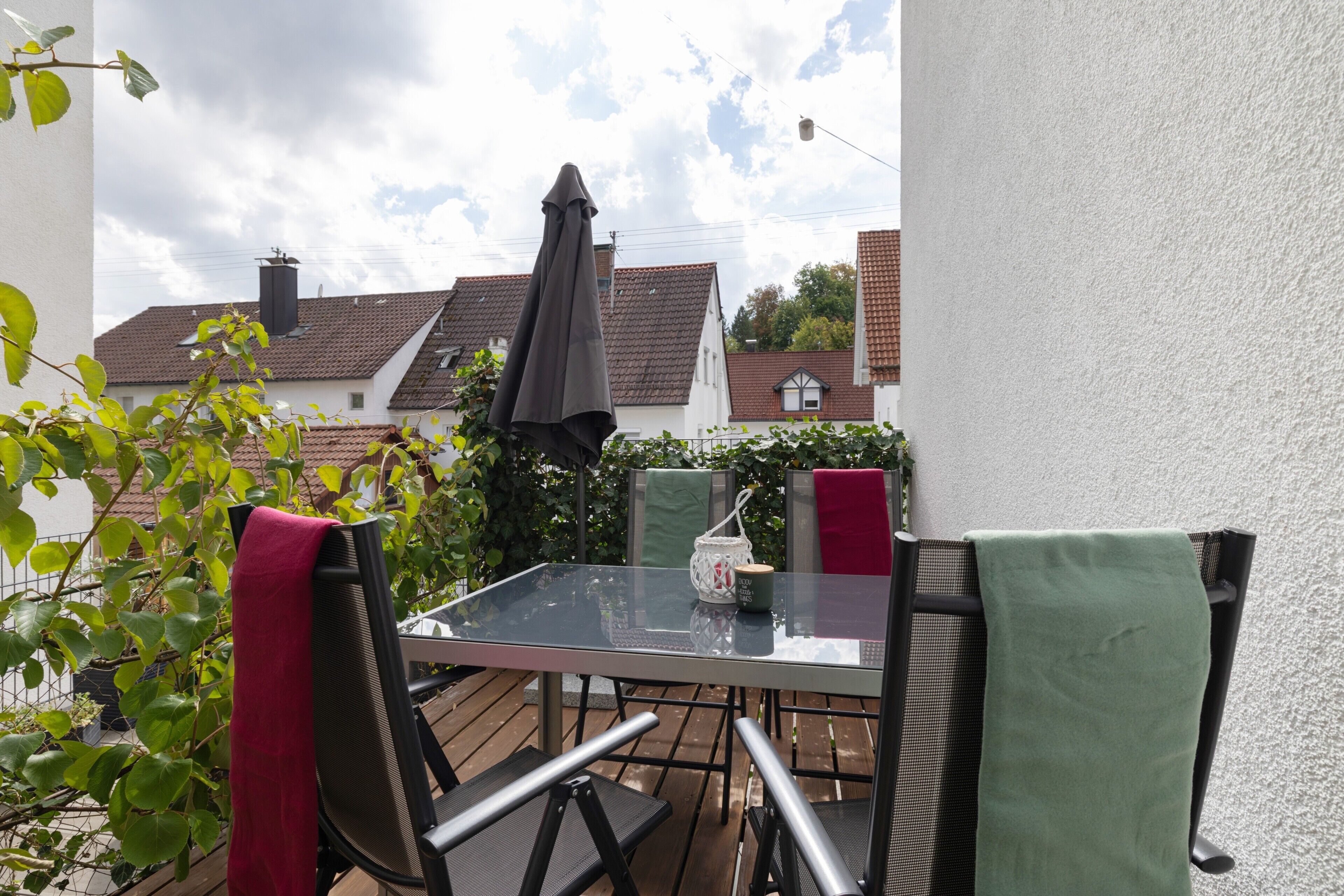 An outdoor patio with a glass table and chairs, a red and green towel, and a white lantern.