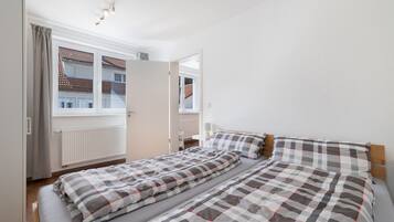 Ein Schlafzimmer mit einem Doppelbett, einem Heizkörper, einem Fenster mit Vorhängen und einer Tür.