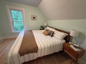 Ein Schlafzimmer mit einem Bett, einem Nachttisch, einer Lampe und einem Fenster.