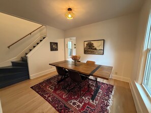 A dining area with a wooden table, chairs, a patterned rug, a staircase, and a painting on the wall. - Cozy 3-bedroom house in the heart of the east side of Madison (Madison)