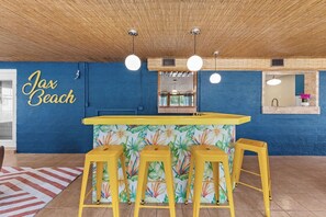 Una zona de bar con pared azul, techo de madera y barra con temática tropical.