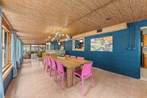 Un comedor con una mesa de madera larga y sillas rosadas, una pared azul decorativa y un techo con diseño tejido.