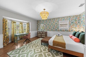 A bedroom with a bed, a desk, a chair, a dresser, a patterned rug, and a window with curtains. - Be A Nomad | The Seabreeze 5BR Pool House (Jacksonville Beach)