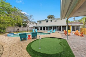 A backyard with a swimming pool, artificial turf, and outdoor furniture. - Be A Nomad | The Seabreeze 5BR Pool House (Jacksonville Beach)