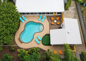 Vista aérea de una zona de piscina con múltiples sillones de descanso y una pequeña terraza verde.
