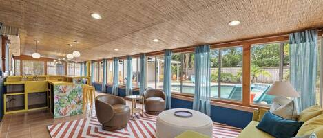 Amplia sala de estar con cocina, ventanas grandes y vista a la piscina.