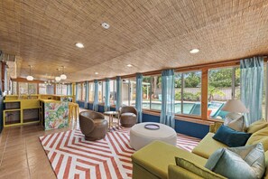 A spacious living area with a kitchen, large windows, and a pool view. - Be A Nomad | The Seabreeze 5BR Pool House (Jacksonville Beach)