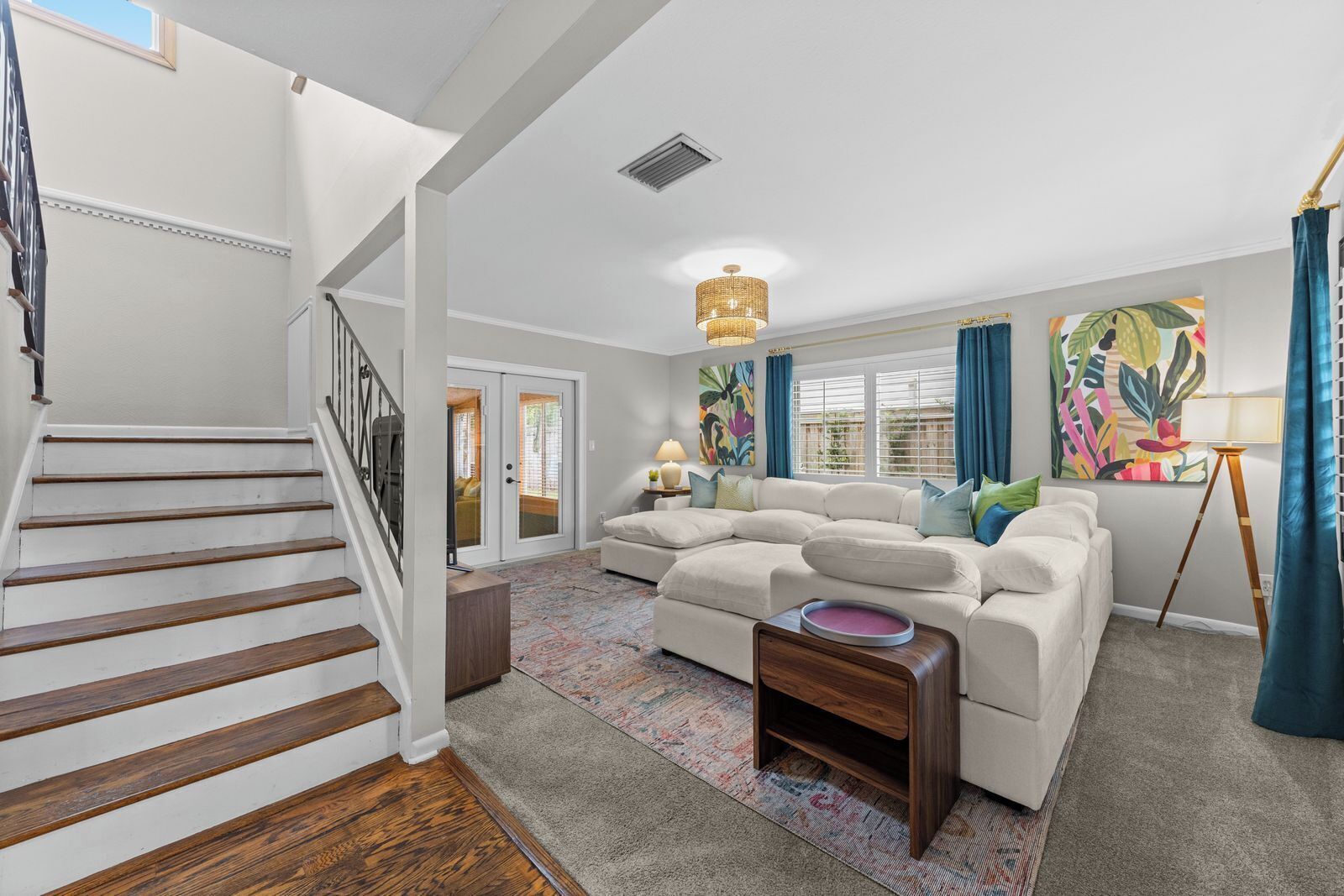 A spacious living room with a staircase, a large sectional sofa, a small side table, and a colorful rug.